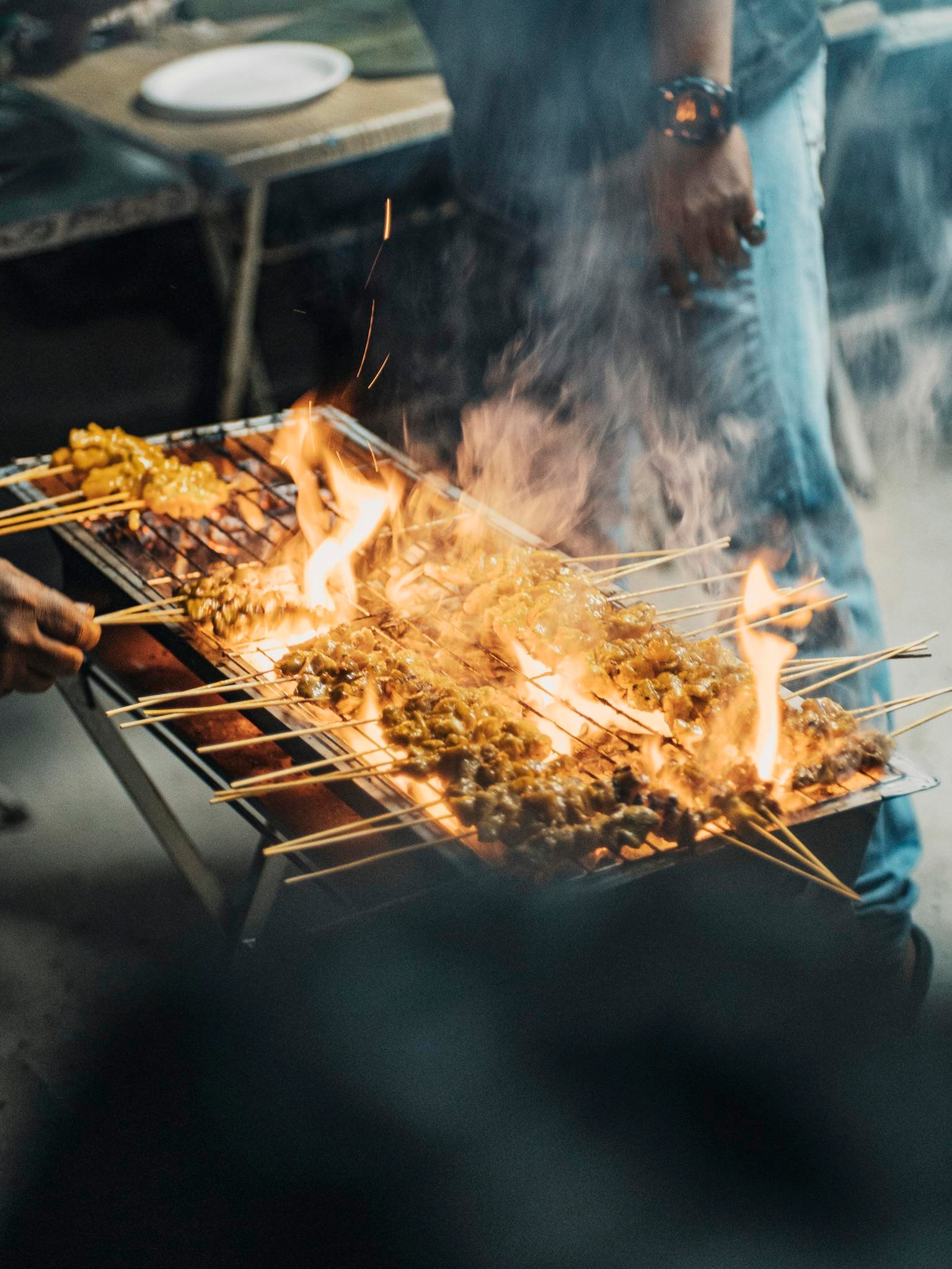 A man grills satay skewers over open flames at a street food stall in Kuala Lumpur, Malaysia.
